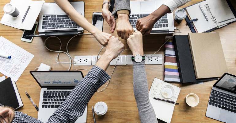 Creative team of web developers and writers giving a fist bump over a meeting table.