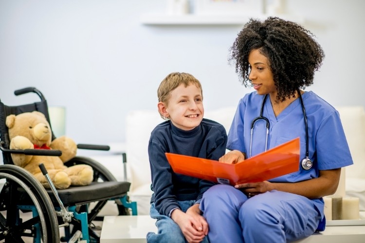 Developmental Disability Nurse reviewing a care plan with a child patient in a wheelchair as part of her job duties.