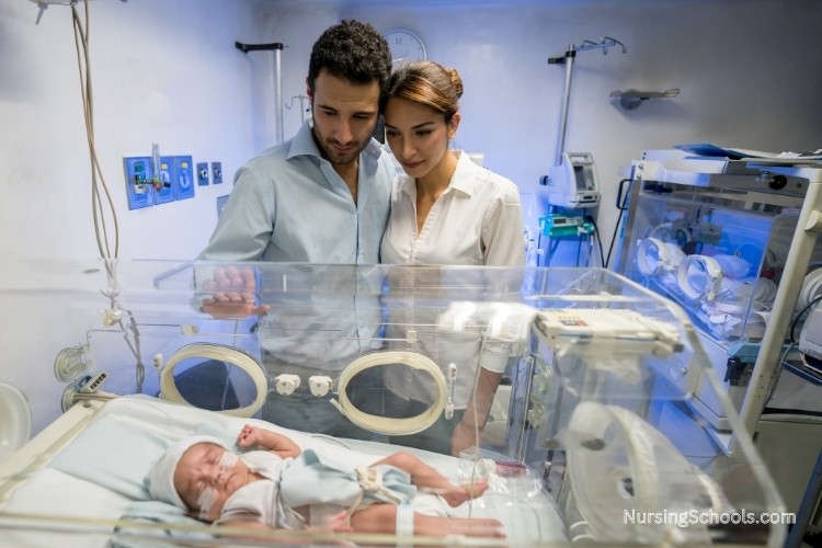Parents looking over a premature baby inside an incubator in the NICU.