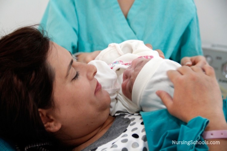 Perinatal Nurse supports the breastfeeding and bonding between the mother and infant in a hospital bed after delivery.